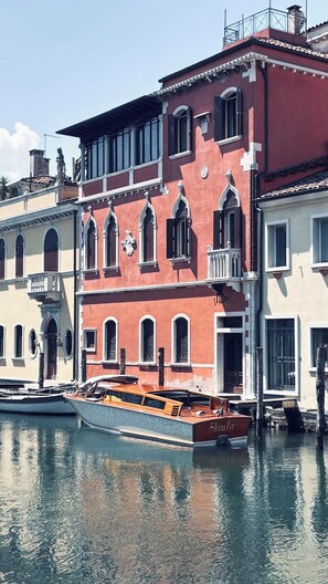 A row of historic Venetian buildings with arched windows and balconies, a boat docked in front, and a clear sky. - Attilia Suite Historical House in Chioggia canal view Vena Laguna di Venezia (Chioggia)