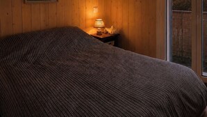 Un dormitorio con cama, una mesita de noche con lámpara, un cartel en la pared y vistas a través de una puerta.