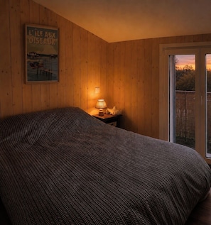 Ein Schlafzimmer mit Bett, Nachttisch mit Lampe, einem Bild an der Wand und Blick durch eine Tür.
