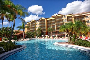 Un hotel con piscina, palmeras y un cielo azul despejado.