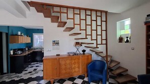 Een kamer met een trap, een blauwe stoel, een houten kast en een keukenhoek.