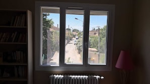 A room with a window overlooking a street, a radiator below the window, and a bookshelf to the left. - Exclusive triple room for 3 people, 1 baby. (Pélissanne)