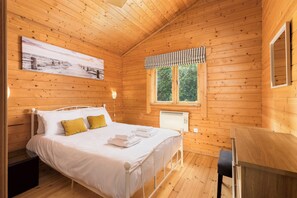 Um quarto de cabana de madeira com uma cama, uma janela, um radiador e uma escrivaninha.