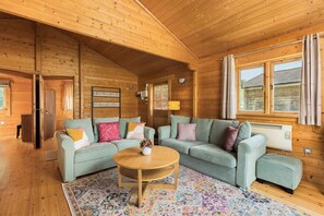 Interior de uma cabana de madeira com sofá de cor verde claro, mesa de centro de madeira e tapete estampado.