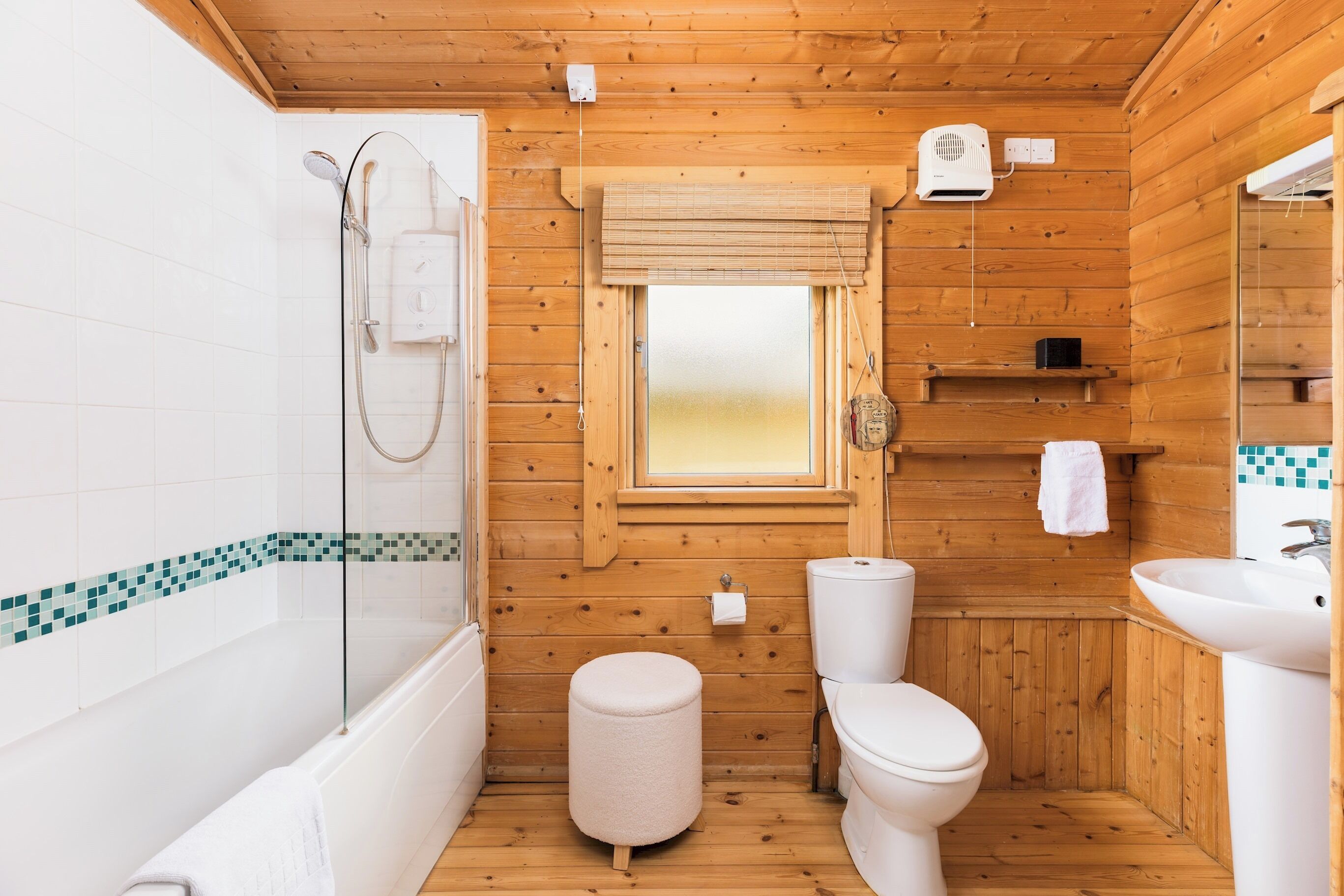 A compact wooden cabin bathroom with a bathtub, toilet, and a small window.