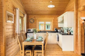 Interior de uma cabana de madeira com uma mesa de jantar, cadeiras, um relógio e uma área de cozinha.