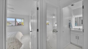 Een slaapkamer met een bed, een badkamer met spiegel en wastafel, en een gang naar een andere kamer.