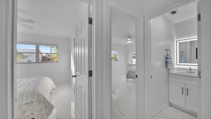 Una camera da letto con un letto, un bagno con uno specchio e un lavandino, e un corridoio che porta a un'altra stanza.
