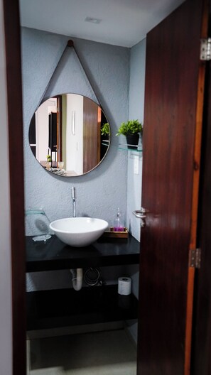 Un baño con un espejo redondo, lavamanos blanco y puerta de madera.