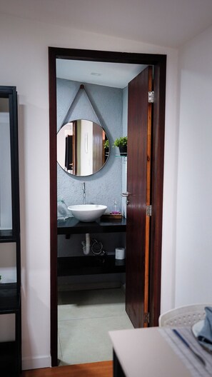 A bathroom with a round mirror, white sink, and wooden door.