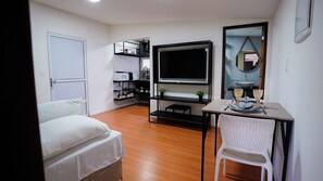 A hotel room with a bed, a TV, a dining table with chairs, a kitchen area, and a bathroom.