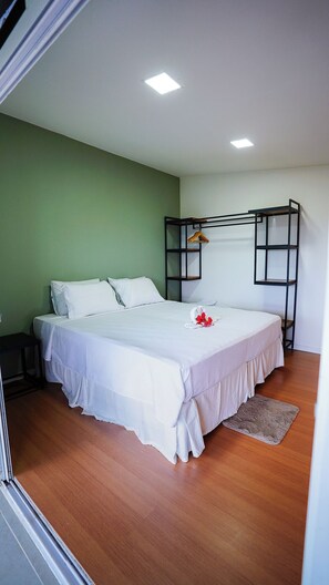 Un dormitorio con una cama, perchero y suelo de madera.