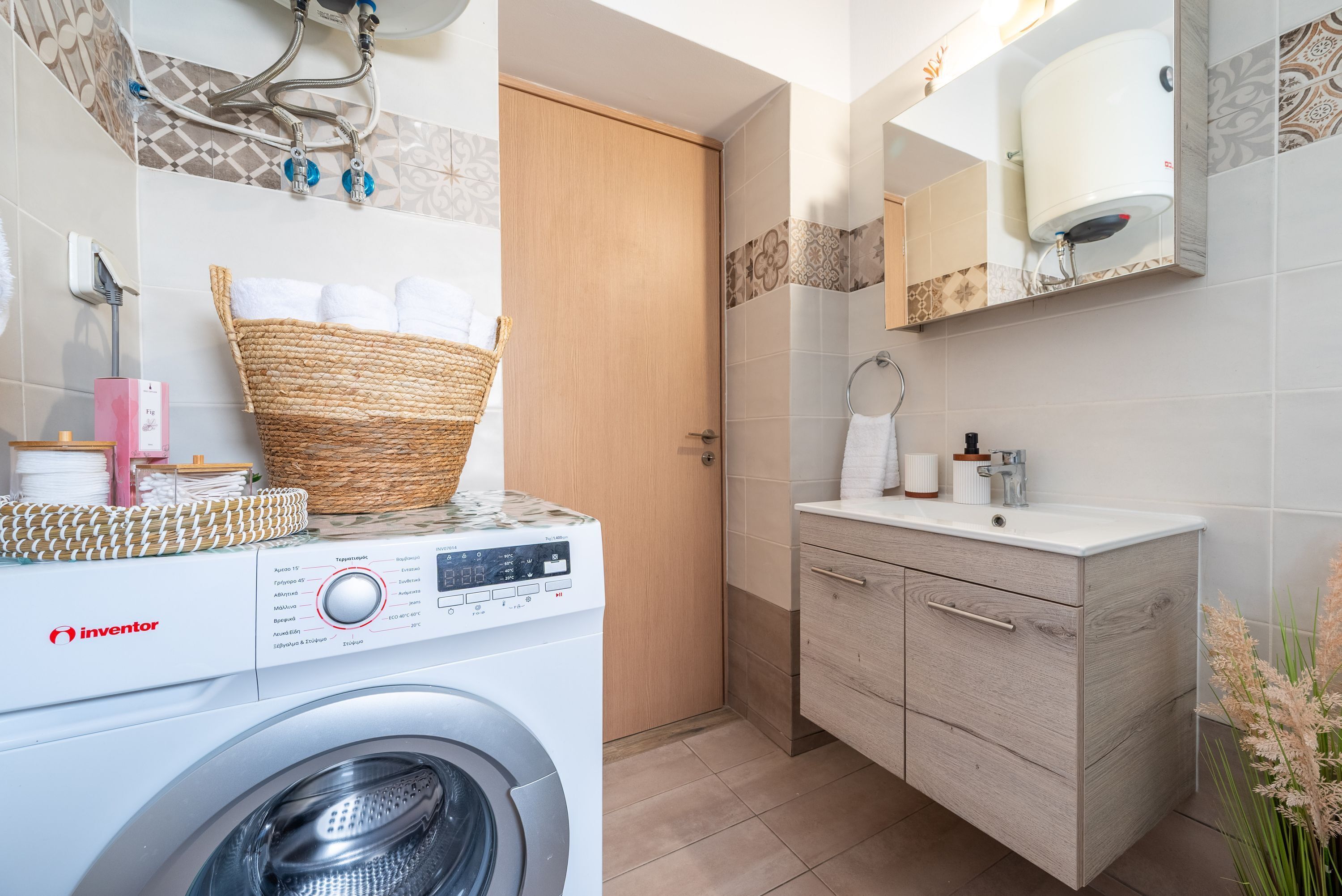 Een moderne badkamer met een wasmachine, een houten deur, een wastafel met spiegel en een handdoekhouder.