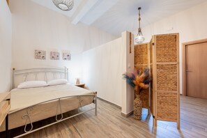 Ein Schlafzimmer mit Bett, Nachttisch, Wandbild, einem gewebten Raumteiler und einer Pendelleuchte.