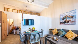 Un espacio moderno de estar con comedor, un conjunto de sofás, un televisor y un cuadro de un barco.