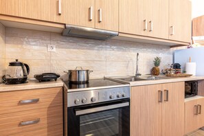 Eine moderne KĂŒche mit Holzausstattung, einem Edelstahlherd, einem Backofen und einer Arbeitsplatte mit Wasserkocher und Topf.