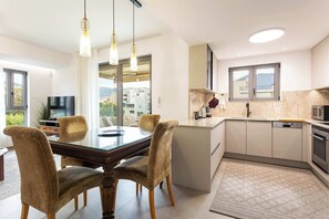 A modern kitchen with a dining area, large windows, and a view of buildings. - Urban Panorama - Stylish Stay in Kalamata (Kalamata)