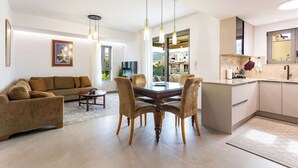 Una sala moderna con un sofá, una mesa de comedor y sillas, una cocina con un fregadero y armarios, y un ventanal con vistas al exterior.