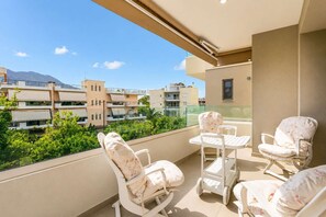 A balcony with white chairs and a table, overlooking a residential area with buildings and greenery. - Urban Panorama - Stylish Stay in Kalamata (Kalamata)