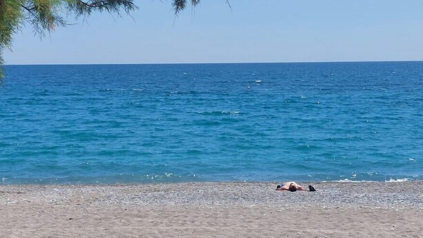 Una playa con una persona recostada en la arena, cielo despejado y mar tranquilo.