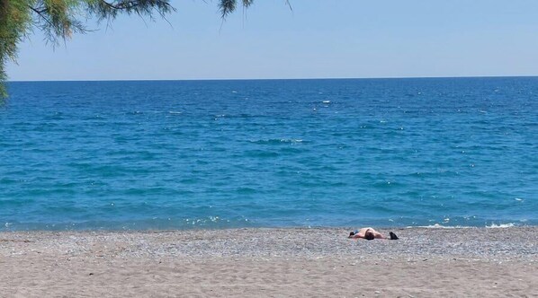 A beach with a person lying on the sand, a clear sky, and calm sea. - Urban Panorama - Stylish Stay in Kalamata (Kalamata)