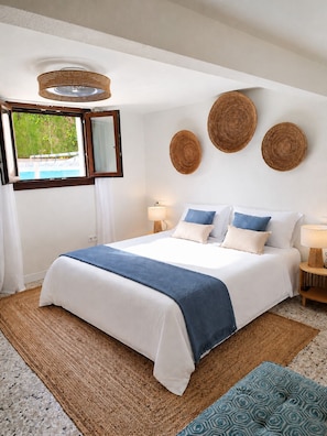 Een keurig opgemaakt slaapkamer met een bed, bedlampen, een raam met uitzicht en decoratieve wandkunst.