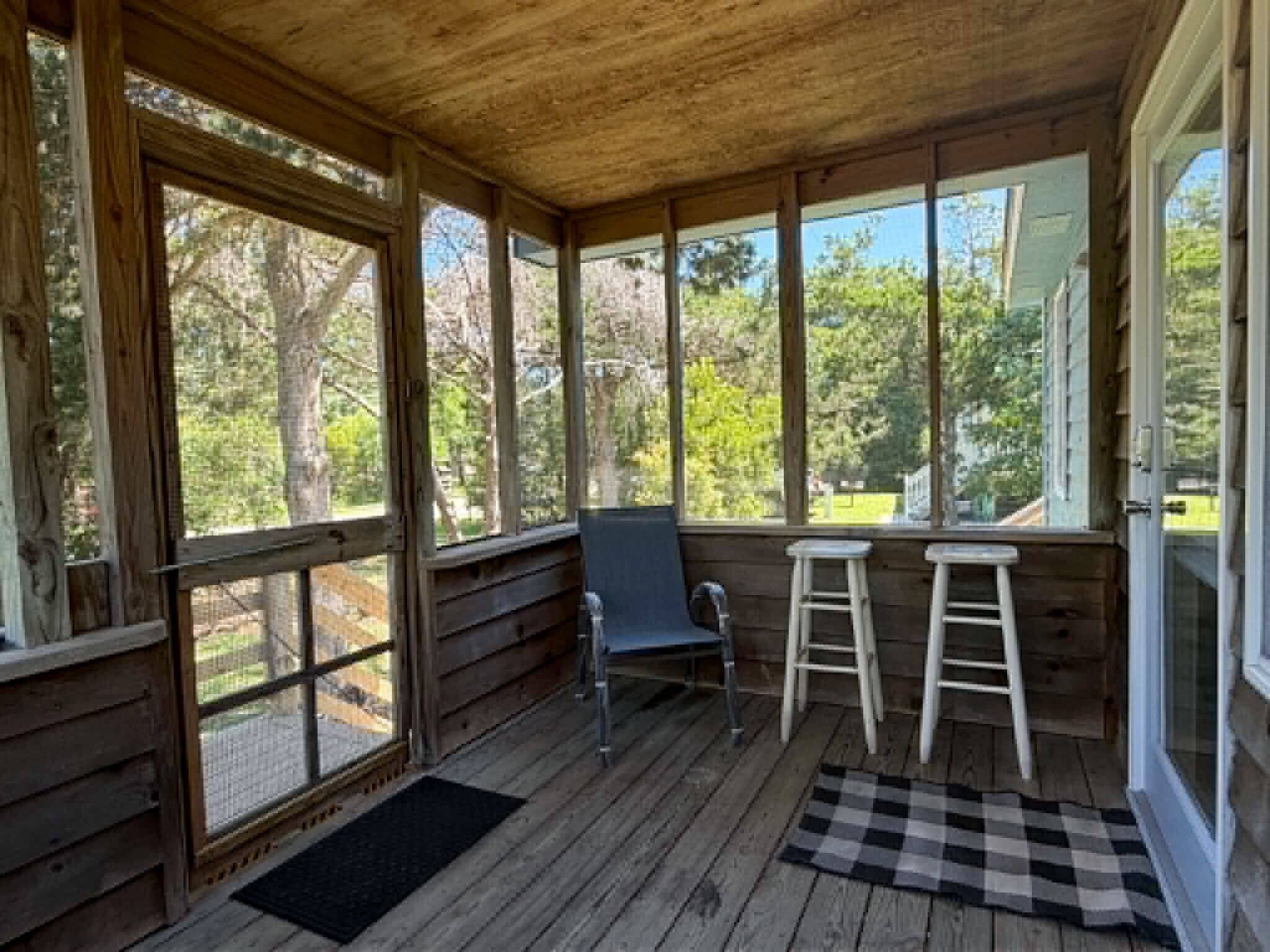 A wooden porch with a bench, two stools, and a checkered rug.