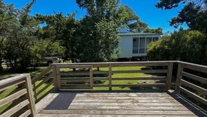 Une terrasse en bois avec une rambarde, une zone herbeuse et une maison en arrière-plan.