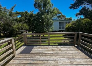 Eine Holzterrasse mit Geländer, eine Rasenfläche und ein Haus im Hintergrund.