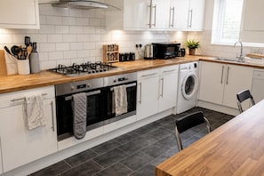 Una cocina moderna con armarios blancos, encimera de madera, cocina a gas, horno, microondas y lavadora.
