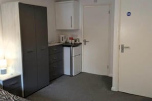 A room with a wardrobe, a small kitchenette, and a door.