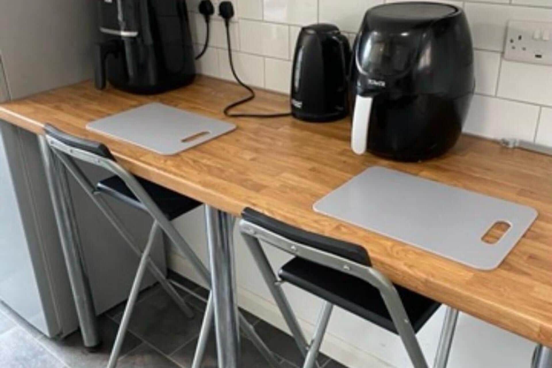 A kitchen with a wooden countertop, two foldable chairs, a coffee maker, and a kettle.