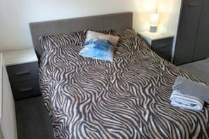 A bed with a zebra print bedspread, a pillow, and a folded towel on a nightstand. - Corby Lodge Park 4-double Bed House Sleeps 8 (Corby)