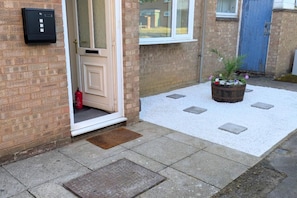 A residential entrance with a mailbox, a door, a window, a blue door, and a potted plant on a gravel path. - Corby Lodge Park 4-double Bed House Sleeps 8 (Corby)