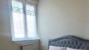 Et soveværelse med en stor seng, et vindue med gardiner, en radiator og en hængende lampe.