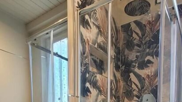 Et badeværelse med en buet hvid vask, et brusekabine i glas og et stort spejl.