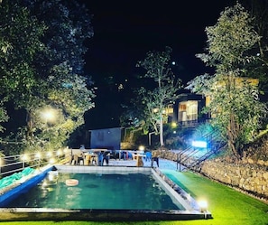 A swimming pool with a stone border, surrounded by a well-maintained lawn and trees. - Bhimtal Hotel nr. Bhowali Range Arahnyam (Bhimtal)