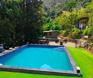 A rectangular pool with a surrounding deck, a small structure with a roof, and a lush green hillside in the background. - Bhimtal Hotel nr. Bhowali Range Arahnyam (Bhimtal)