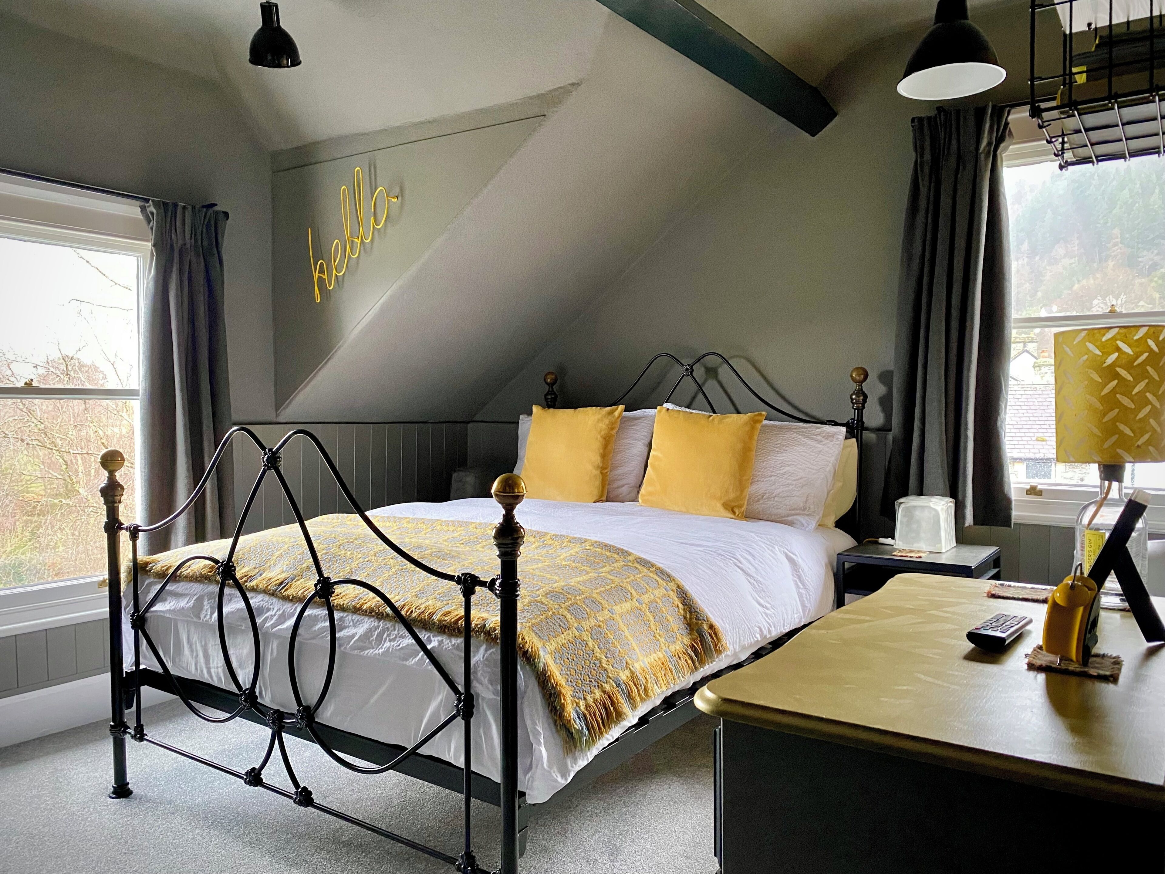 A bedroom with a bed, bedside table, lamp, and a neon sign on the wall.