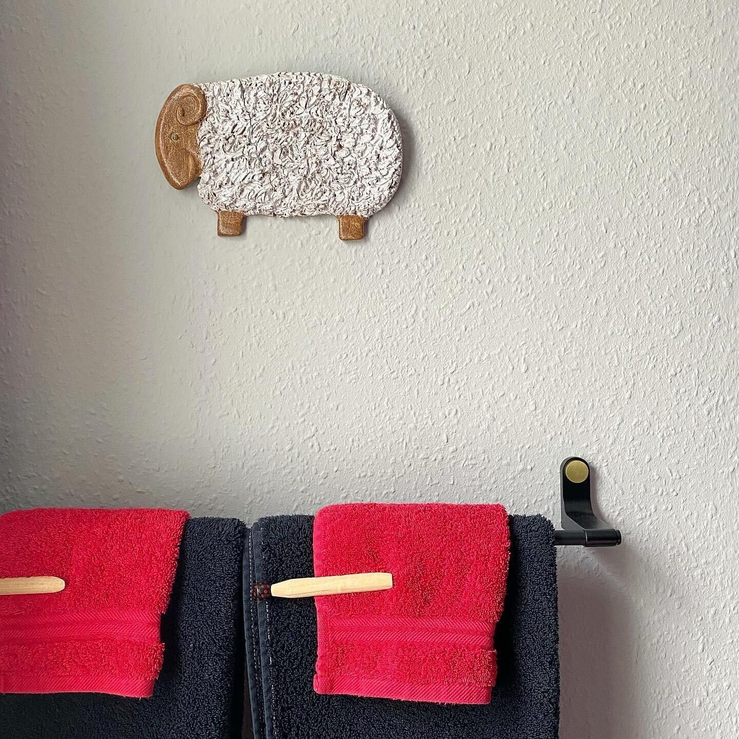 Um porta-toalhas com duas toalhas, uma vermelha e uma preta, e uma decoração de ovelha presa à parede.