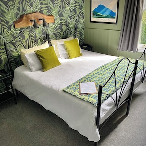 A bed with white bedding, a green and blue patterned throw, and a wooden headboard.