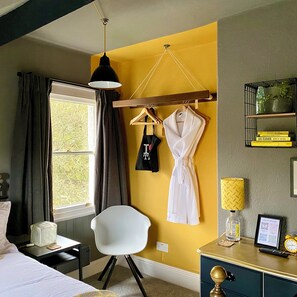 A hotel room with a bed, a desk with a lamp, a chair, a robe hanging on a rack, and a window with curtains.