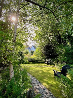 A garden with a bench, a pathway, and a house in the background.