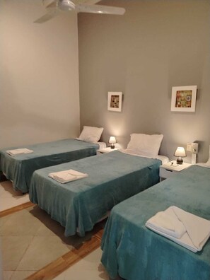 Une chambre d’hôtel avec deux lits simples, un ventilateur de plafond, des lampes de chevet et deux tableaux encadrés accrochés au mur.