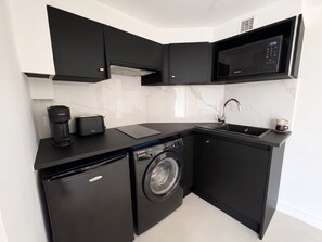 Una cocina compacta equipada con microondas, tostadora, cafetera, lavabo y lavadora.