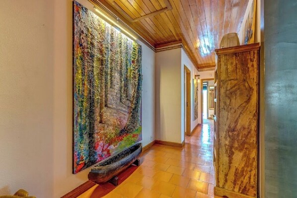 A hallway with a large abstract painting on the wall, wooden flooring, and a wooden cabinet.