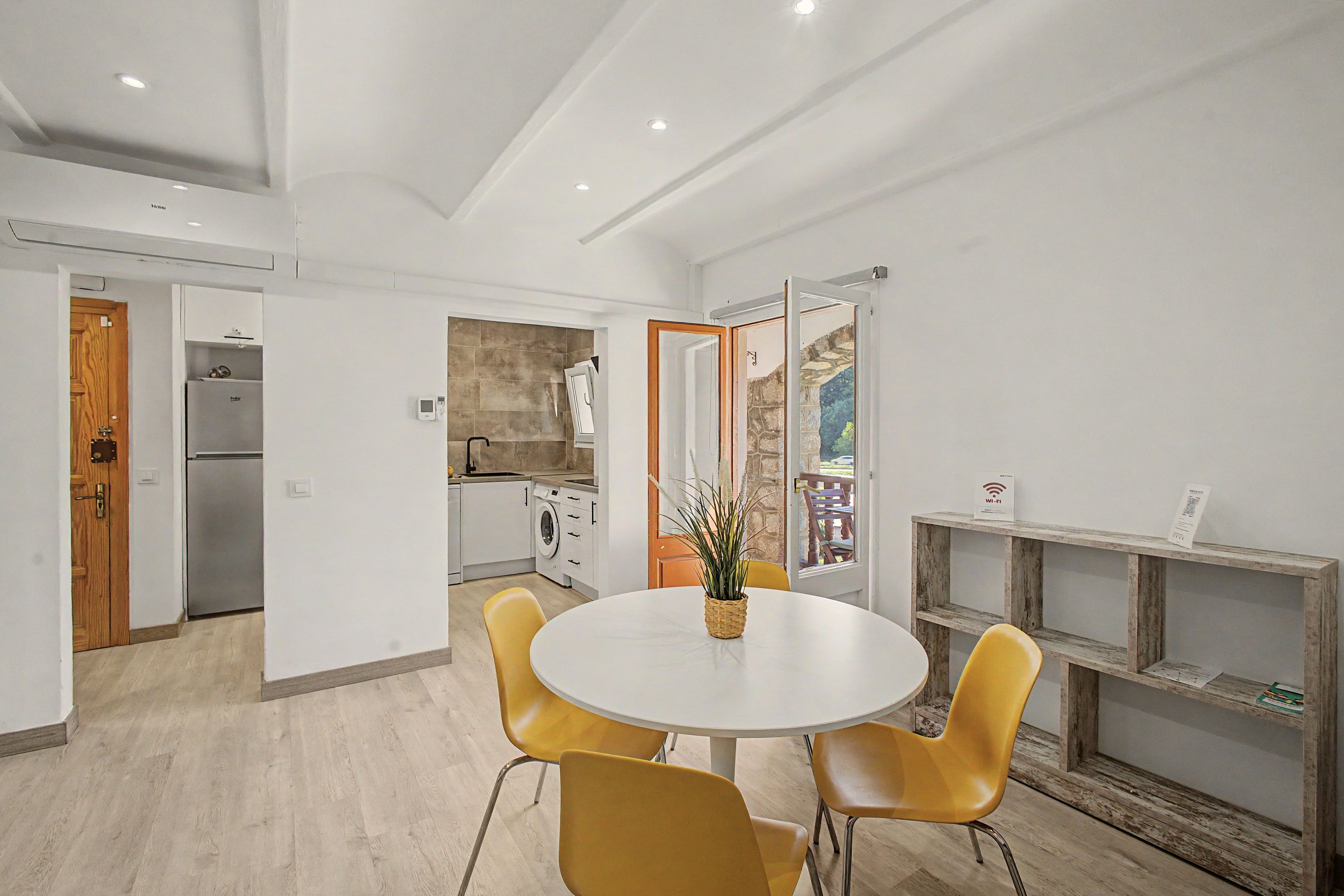 Una cocina moderna con armarios blancos, lavadora integrada y un comedor con una mesa redonda y sillas amarillas.