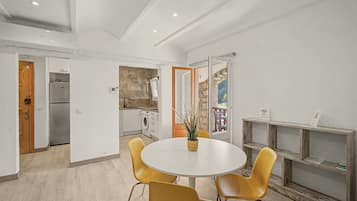 Una cocina moderna con armarios blancos, lavadora integrada y un comedor con una mesa redonda y sillas amarillas.