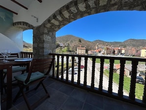 Un balcon agrémenté d’une arche en pierre, une table avec des chaises et une vue sur la ville et les montagnes.