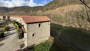 Un bâtiment en pierre avec un toit recouvert de tuiles rouges, un chemin pavé et une rivière.